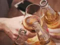 Ludzie wznoszą toast butelkami piwa i kieliszkiem alkoholu.