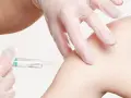 Ręka w rękawiczce medycznej wykonuje zastrzyk w ramię.