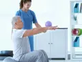 Fizjoterapeutka pomaga starszemu mężczyźnie ćwiczyć na piłce rehabilitacyjnej.
