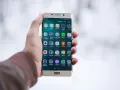 Dłoń trzymająca złoty telefon Samsung z ikonami aplikacji na ekranie.