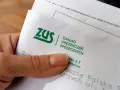 Dłoń trzyma dokument z logo ZUS i napisem "Zakład Ubezpieczeń Społecznych".