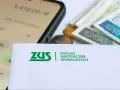 ZUS, pieniądze, monety i kalkulator na ekranie telefonu.