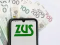 ZUS świadczenie wspierające na ekranie telefonu, otoczone polskimi banknotami.