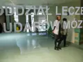 Drzwi do oddziału leczenia udarów mózgu. W środku widać personel medyczny i pacjentów, gotowych na zabiegi takie jak trombektomia.