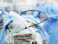 Pacjent na stole operacyjnym, przygotowany do zabiegu PCI kardiologia. W tle personel medyczny w niebieskich fartuchach.