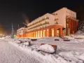Budynek sanatorium nocą, ośnieżony teren z ławkami i drzewami.