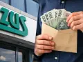 Logo ZUS i ręce trzymające kopertę z polskimi banknotami 100 zł.