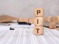 Drewniane kostki z literami PIT ułożone na dokumentach podatkowych.