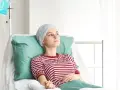 Młoda kobieta w chuście na głowie leży w szpitalnym łóżku, podłączona do kroplówki.