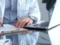 Lekarz w białym kitlu pisze na dokumentach, obok laptop. Zastanawia się, ile można być na zwolnieniu lekarskim od psychiatry.