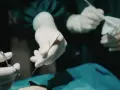 Dłonie chirurga w rękawiczkach trzymające narzędzia chirurgiczne i gazę podczas operacji.