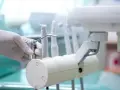 Dłoń w rękawiczce trzymająca końcówkę stomatologiczną na tle sprzętu dentystycznego.
