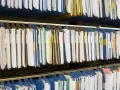 Rzędy wiszących segregatorów, gotowych do archiwizacji dokumentów. Widać tu wiele teczek, niektóre z kolorowymi etykietami, idealne do organizacji pracy, np. z wykorzystaniem systemu druk erp-6.