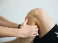 Fizjoterapeuta bada kolano pacjenta, dotykając jego bocznej części.