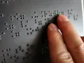 Dłoń czytająca tekst Braille'a na czarnej powierzchni.