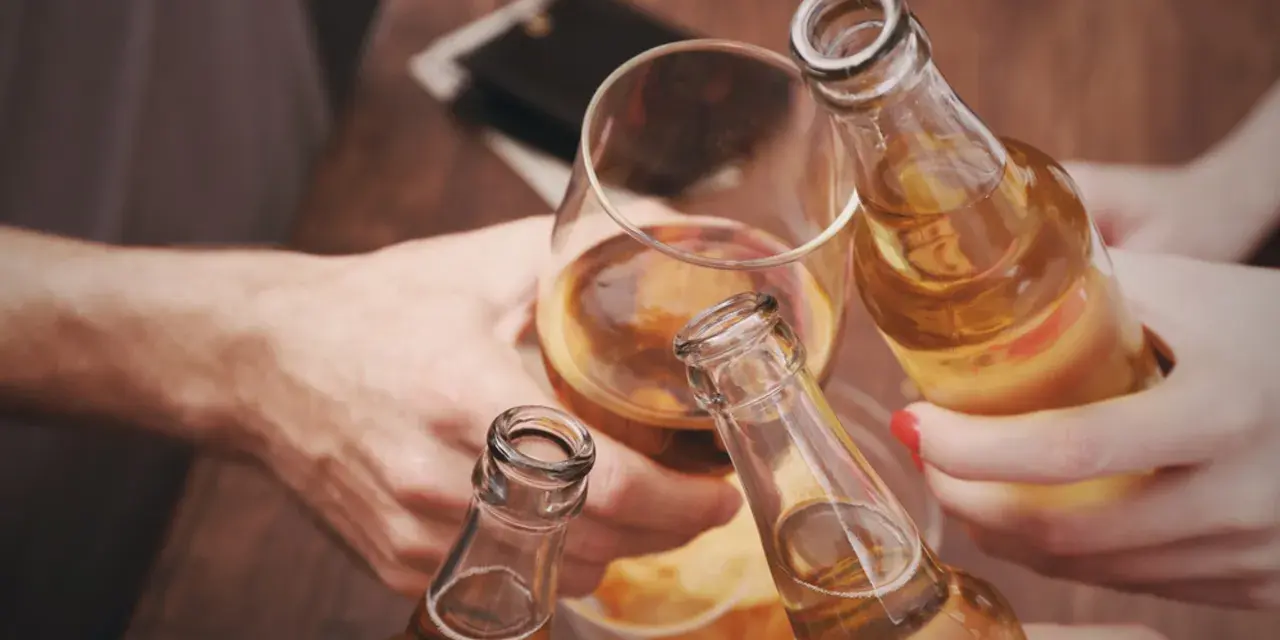 Ludzie wznoszą toast butelkami piwa i kieliszkiem alkoholu.
