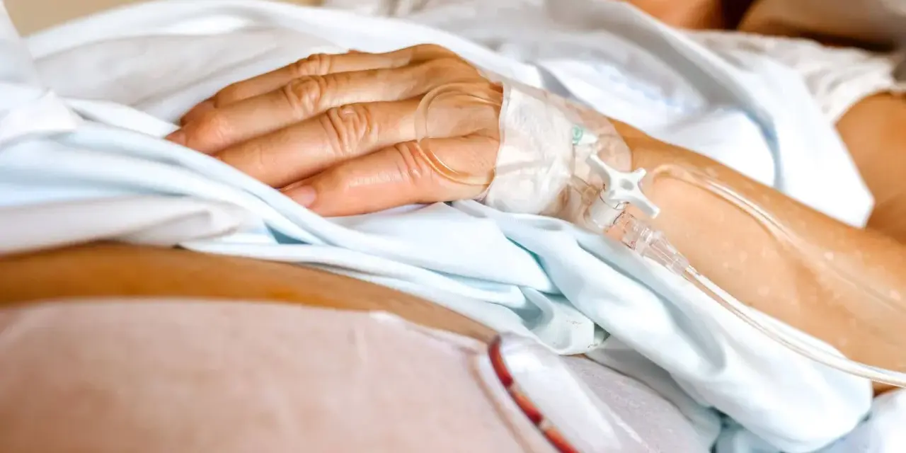 Dłoń pacjenta z wenflonem, przygotowująca się do podróży ze szpitala do hospicjum.
