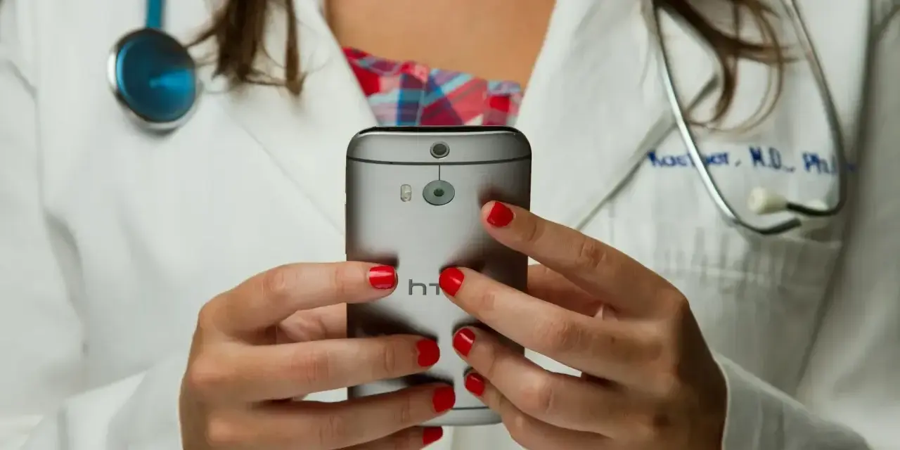Lekarz w białym kitlu trzyma smartfon, na którym widać aparat i logo HTC.