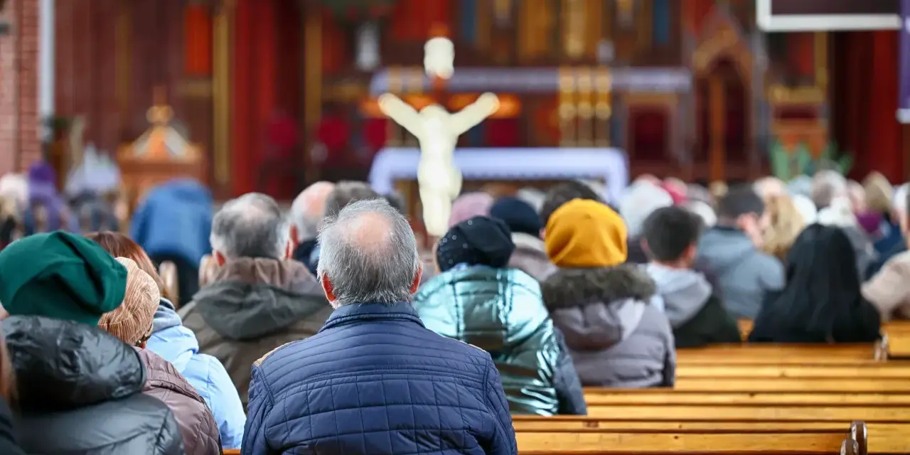 Ludzie siedzący w kościele, widok od tyłu, w tle ołtarz z krzyżem.