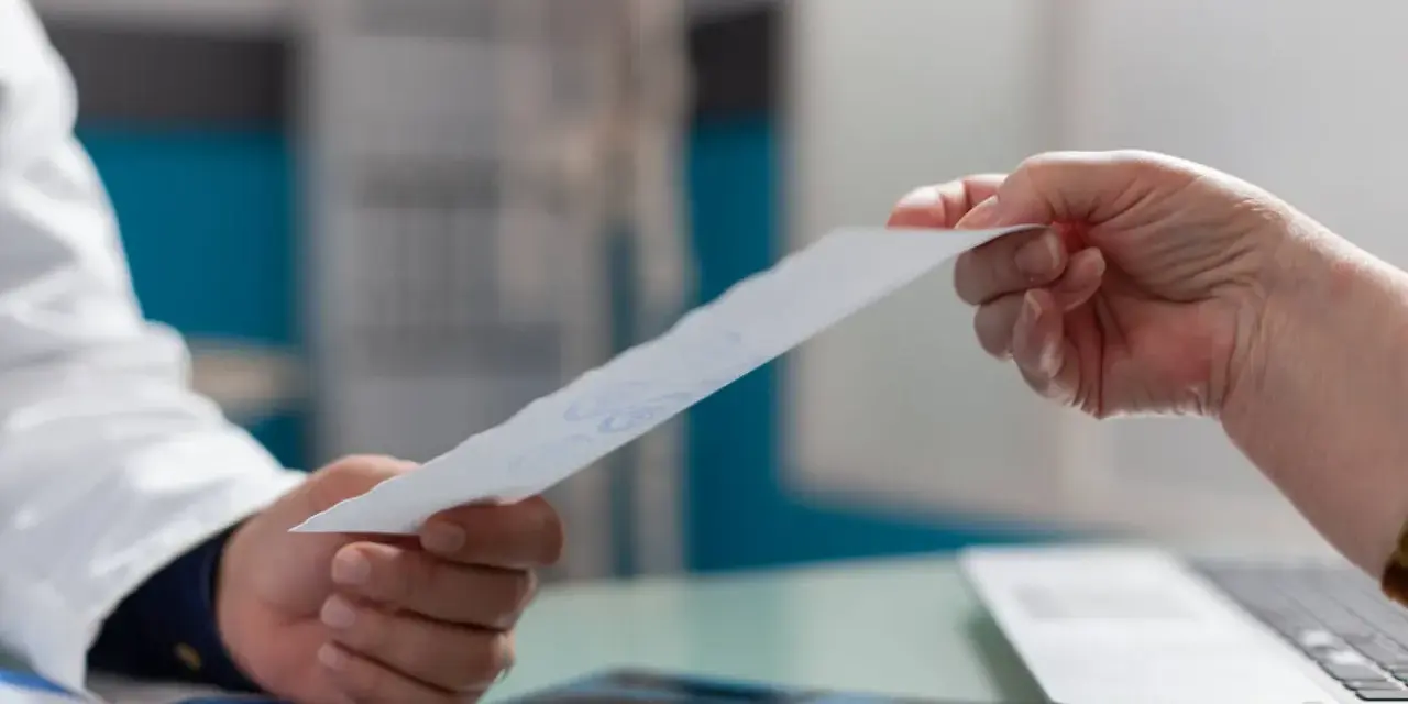 Lekarz w białym fartuchu podaje pacjentowi dokument.