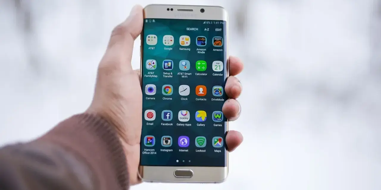 Dłoń trzymająca złoty telefon Samsung z ikonami aplikacji na ekranie.
