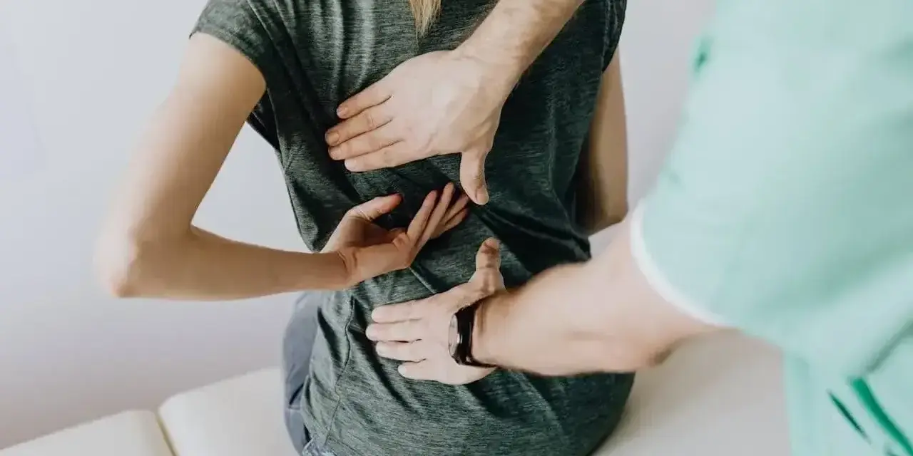 Fizjoterapeuta bada plecy pacjentki. Lekarz lub fizjoterapeuta wystawia zwolnienie na czas rehabilitacji.