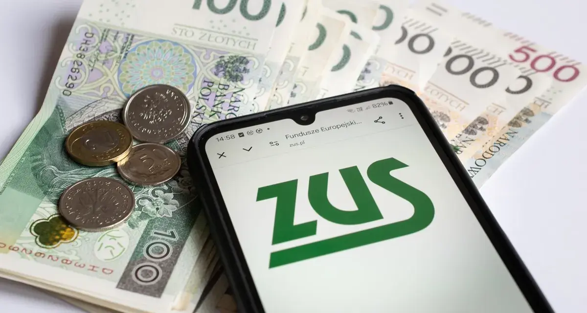 Telefon z logo ZUS na tle polskich banknotów i monet.