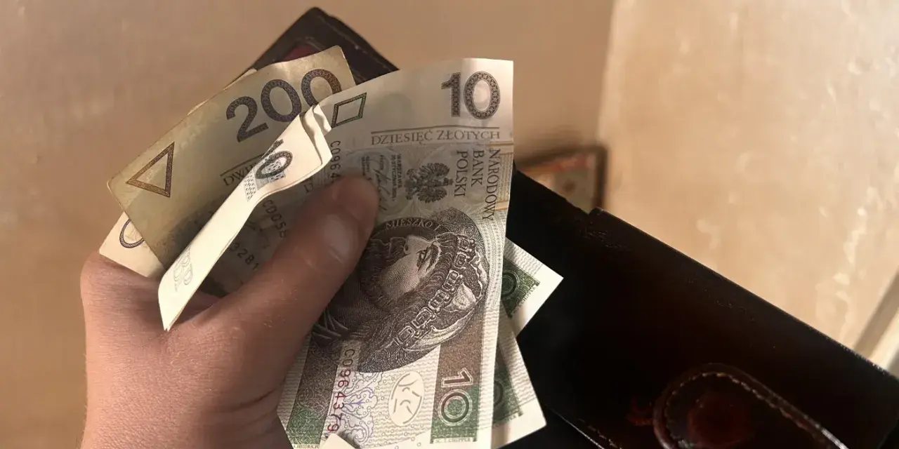 Dłoń trzyma polskie banknoty 10 zł i 200 zł obok portfela.