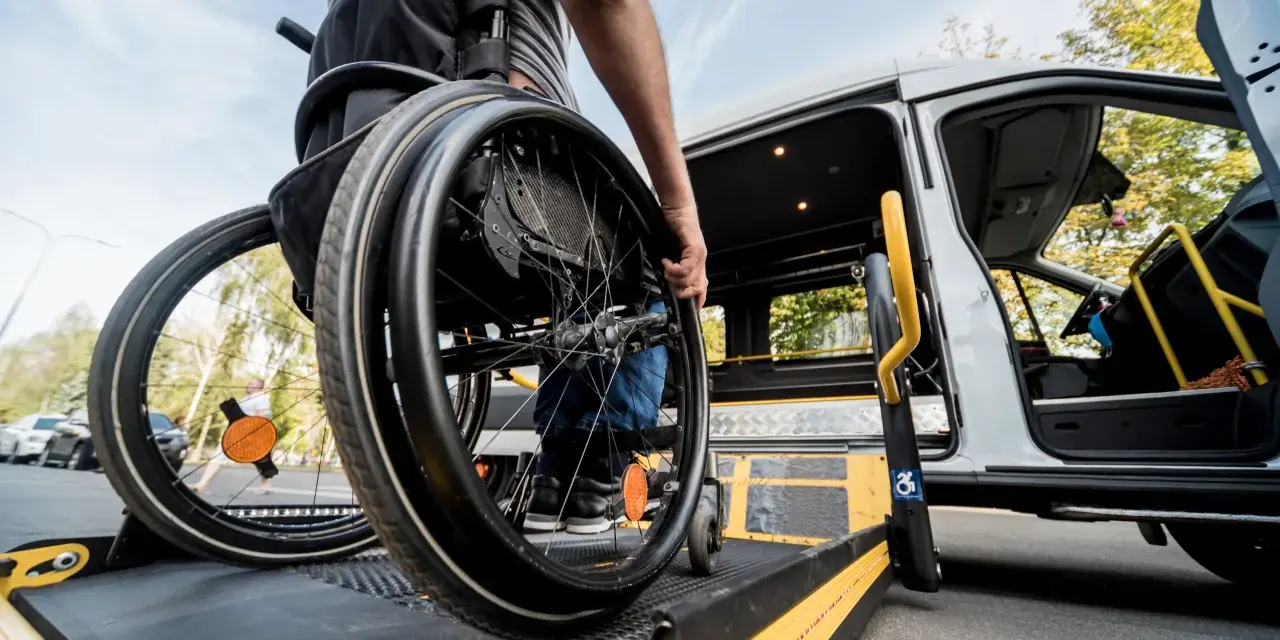 Osoba na wózku inwalidzkim wjeżdża na podjazd przystosowanego busa.