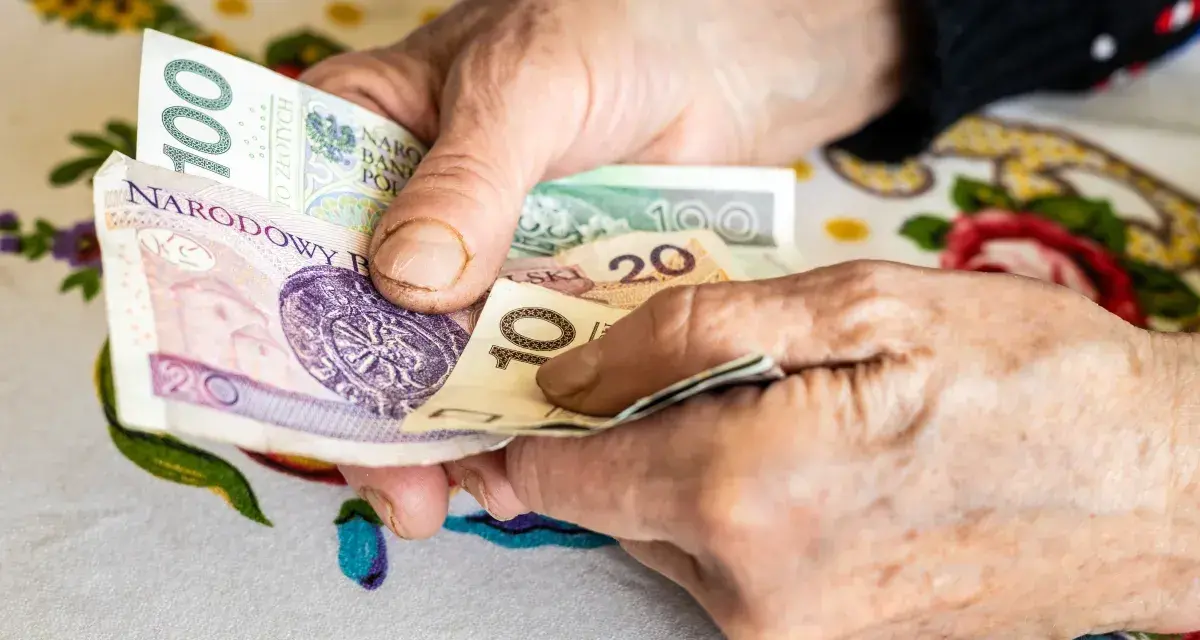 Dłonie starszej osoby liczą pieniądze. Może to być dodatek opiekuńczy po 80 roku życia, zapewniający wsparcie finansowe.