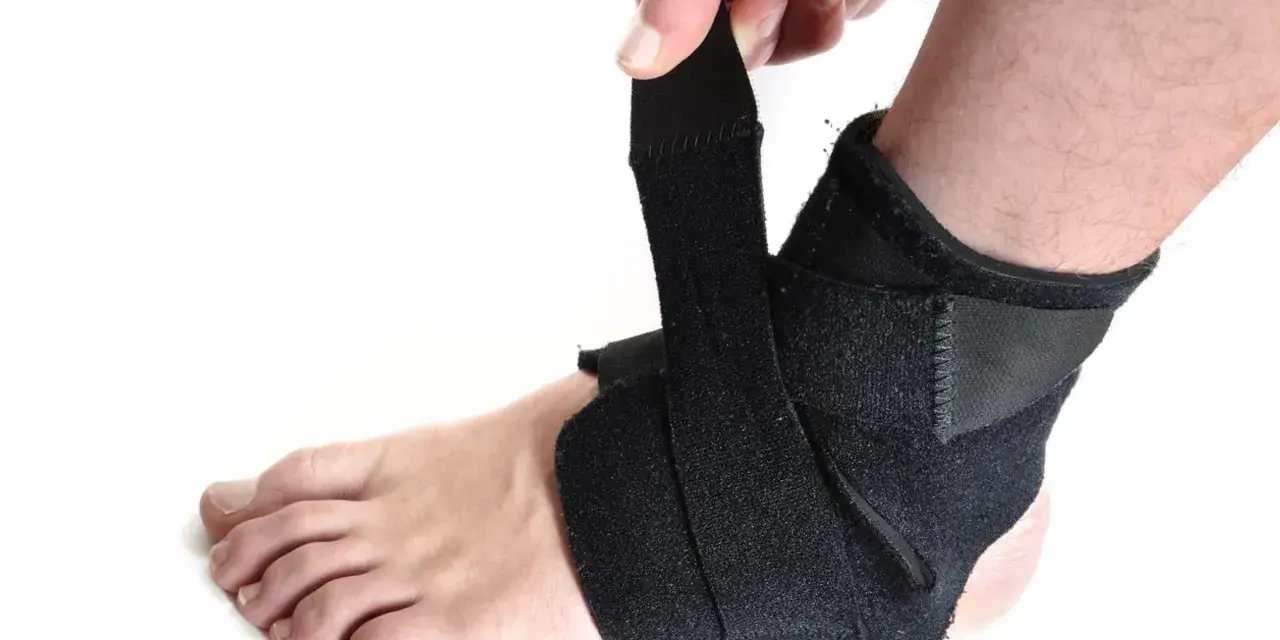 Dłoń zapina czarną ortezę na stopie i kostce.