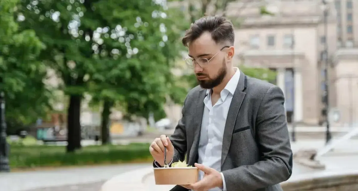 Mężczyzna w garniturze je sałatkę na zewnątrz.