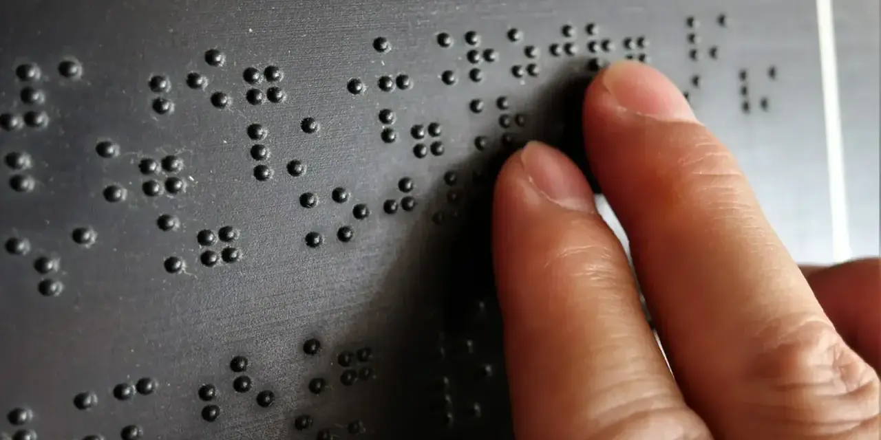 Dłoń czytająca tekst Braille'a na czarnej powierzchni.