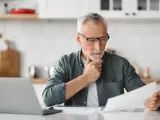 Emeryt zamyślony nad dokumentami, zastanawia się, czy emeryt może ubezpieczyć dorosłe dziecko. Obok laptop.