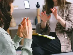 Dwie kobiety rozmawiają w gabinecie, jedna gestykuluje.