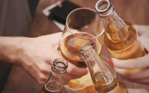 Ludzie wznoszą toast butelkami piwa i kieliszkiem alkoholu.