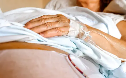 Dłoń pacjenta z wenflonem, przygotowująca się do podróży ze szpitala do hospicjum.