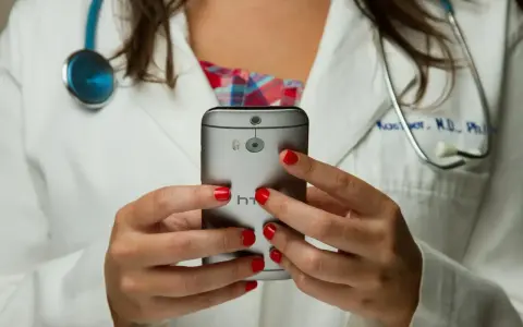 Lekarz w białym kitlu trzyma smartfon, na którym widać aparat i logo HTC.