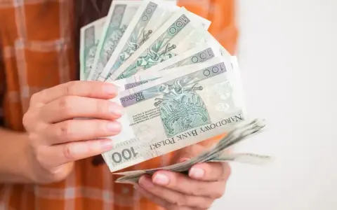 Dłonie trzymające stos banknotów 100 zł. Może to być symbol wsparcia, np. zasilek dla bezrobotnych.