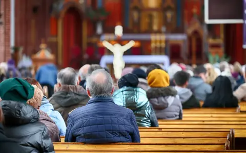 Ludzie siedzący w kościele, widok od tyłu, w tle ołtarz z krzyżem.