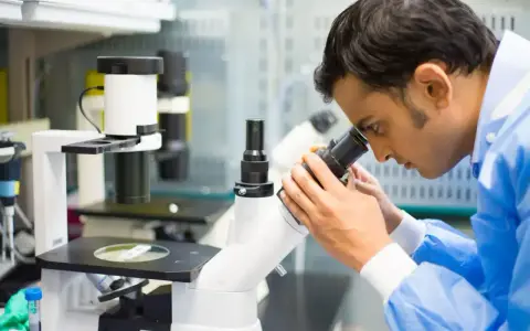 Mężczyzna w niebieskiej fartuchu laboratoryjnym bada próbkę pod mikroskopem, kluczowy element w diagnostyce patomorfologia.