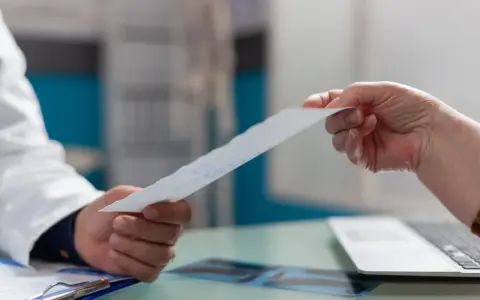 Lekarz w białym fartuchu podaje pacjentowi dokument.