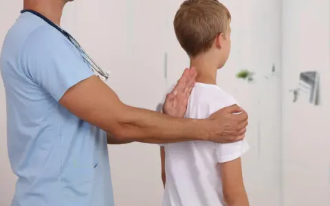 Lekarz bada chłopca, sprawdzając jego postawę. Może to być część diagnostyki zespołu Marfana objawy.