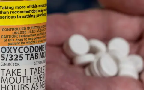 Butelka z lekiem Oxycodone i garść tabletek w dłoni.