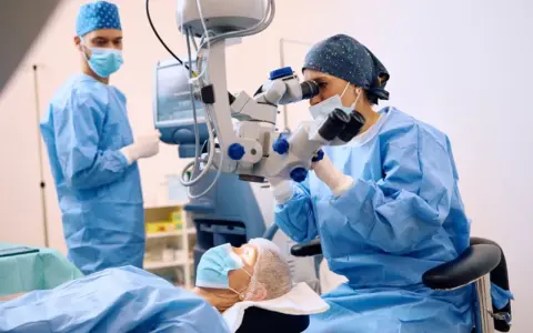 Chirurdzy w maseczkach i fartuchach operują pacjenta przy użyciu mikroskopu.