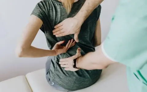 Fizjoterapeuta bada plecy pacjentki. Lekarz lub fizjoterapeuta wystawia zwolnienie na czas rehabilitacji.