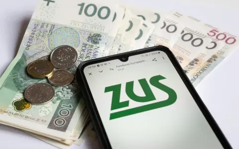 Telefon z logo ZUS na tle polskich banknotów i monet.
