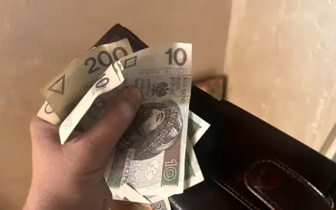 Dłoń trzyma polskie banknoty 10 zł i 200 zł obok portfela.