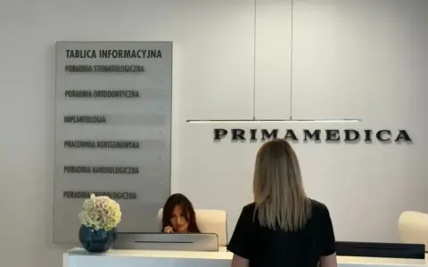 Recepcja gabinetu stomatologicznego Primamedica z tablicą informacyjną i pracownicą.