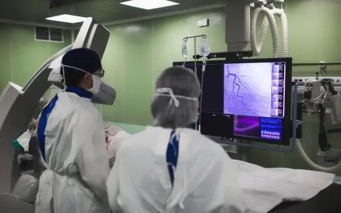 Lekarze w sterylnym stroju analizują obraz z koronarografii na monitorze w sali operacyjnej.